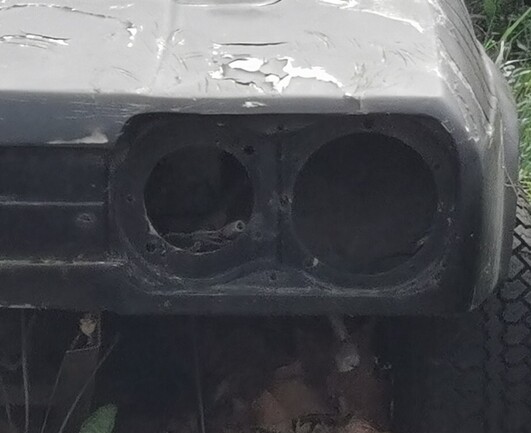 Front left hand corner of a black car in poor condition. The headlamp is missing as is the bumper. The car would have a dual headlamp if it was there. 