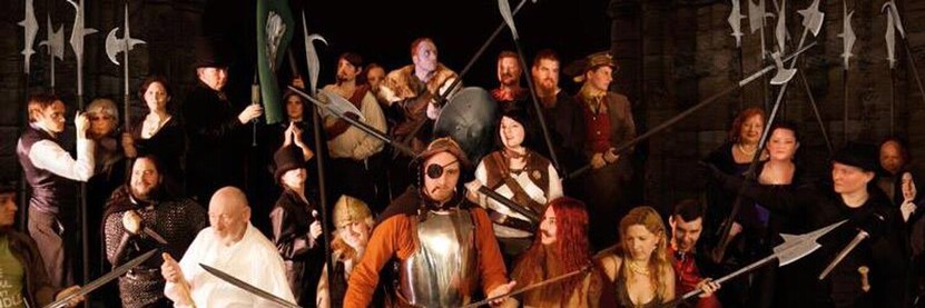 A photograph of a group of fans recreating the Night Watch book cover - people are dressed in costumes of Watch members and other Discworld characters. Pikes and a black background have been digitally added.