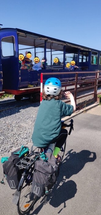 A photo of 7 year old Conan cycling from Cork to Dublin, waving at some fellow kids who are passing by in a teeny train.