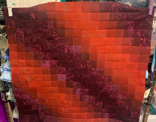 Vibrant red and purple squares sewn together to make an ombré fabric pattern. 