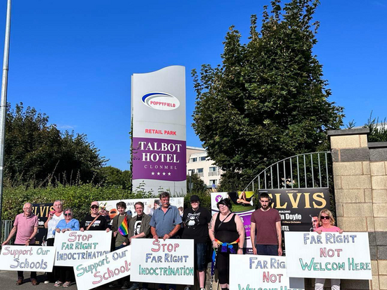 Photo of a group of 11 people standing outside The Talbot Hotel in Clonmel in Tipperary carrying signs saying Stop Far Right Indoctrination, d