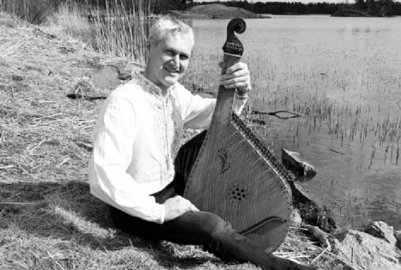 A black and white photo of Ihor Subotyak, siting by a river with a traditional musical instrument  in his hand