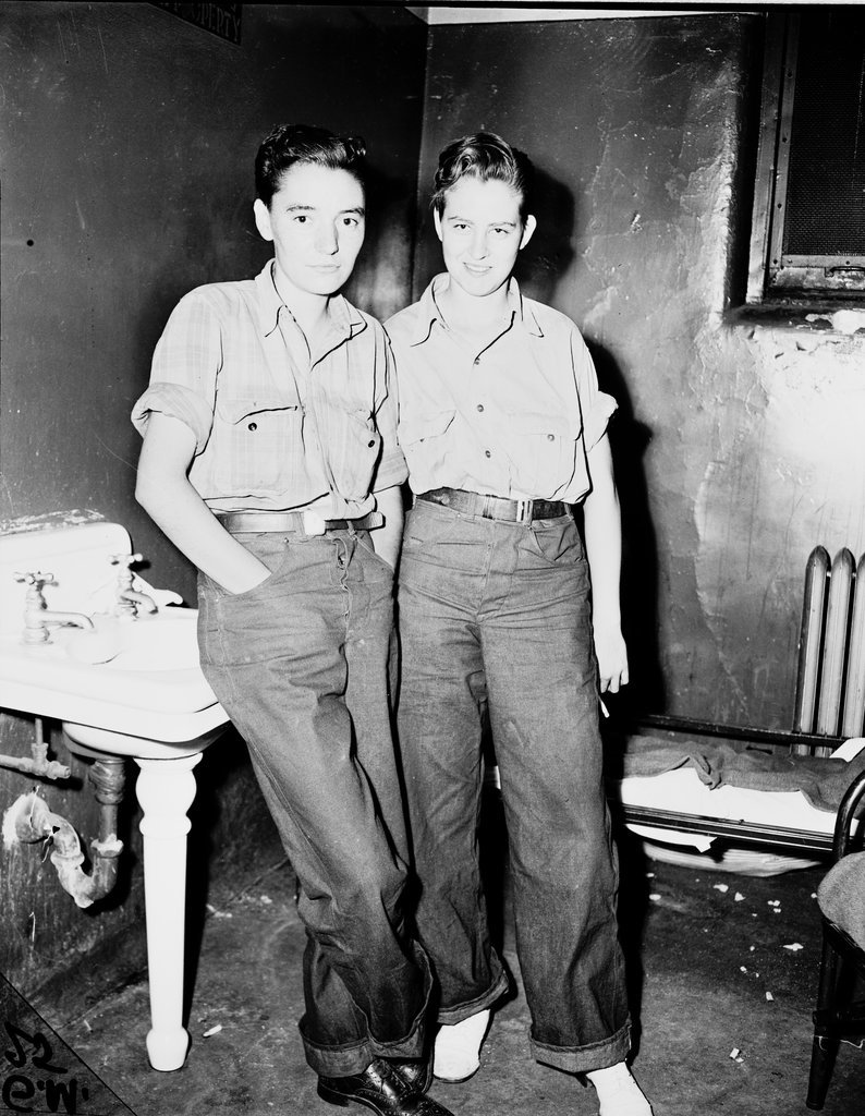 Two young women dressed in jeans and shirts, standing next to a sink in what may be a holding cell.