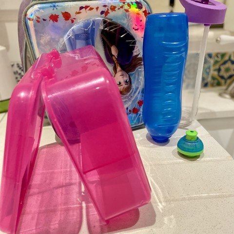 Assorted plastic containers on a counter, with a reflective surface revealing a Frozen’s Anna’s upside-down face.