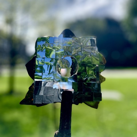 An abstract sculpture of a human figure made of mirrored surfaces in a park setting.