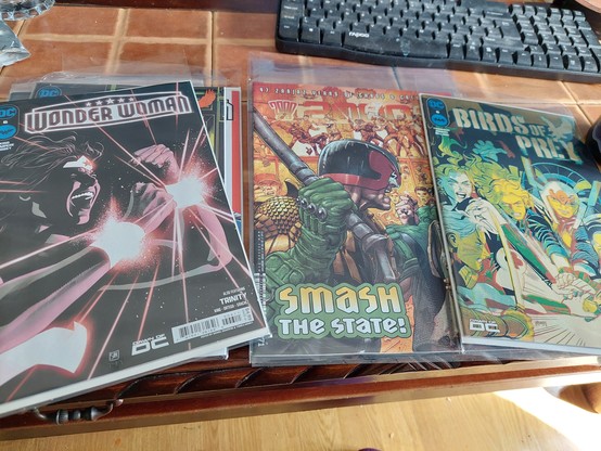 Photo of comics in protective plastic sleeves, on a coffee table. 2000AD, wonder woman and birds of prey. 