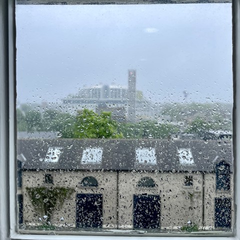 Raindrops on a window with blurred buildings in the background.