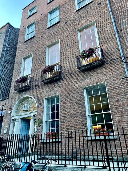 James Joyce Centre, North Great George’s Street. A Georgian brown brick building with multiple windows adorned with flower boxes, an arched doorway, and a black metal fence. Bicycles are parked in front.