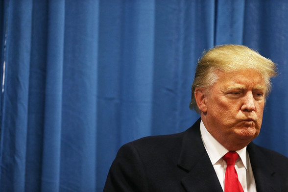 A scowling Donald Trump set against a blue curtain backdrop 