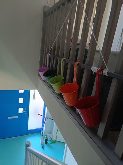 Colourful pots hanging from grey pole held up by macrame strings. 