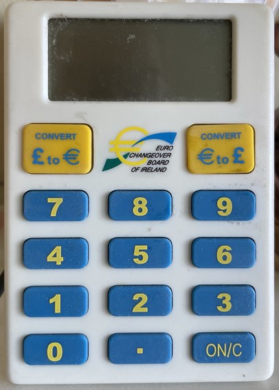 Image of a currency converter device with a keypad. The device features buttons for converting between Irish punt/ pounds (£) and euros (€), displaying the Euro Changeover Board of Ireland logo. The screen is blank.