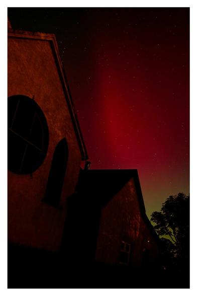 Red and green night skies over a church and trees.