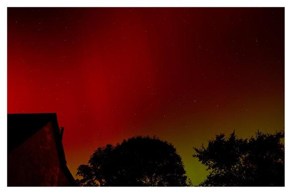 Red and green night skies over a church and trees.