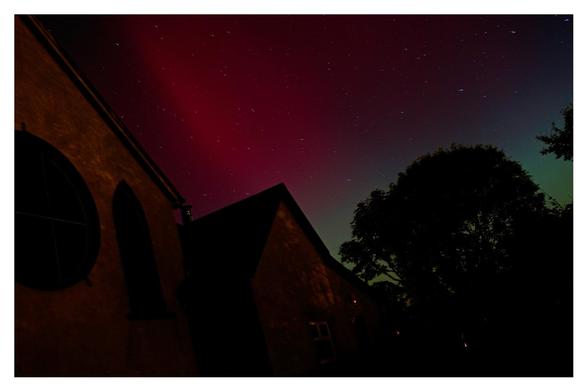 Red and green night skies over a church and trees.
