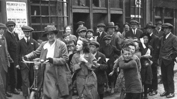 Constance Markievicz wheeling her bicycle, followed by a crowd of girls and boys