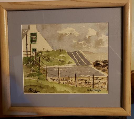 Small watercolor painting of a flat grey roof, and small hill with white house and green wooden windows, also grey and white clouds and brown rocks below a grey sea.