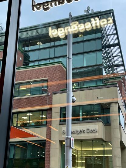 Photo of a modern office building with large glass windows and a brick facade. Notable signage reads "6 George’s Dock." A streetlight and reflections of neon signage and strip lights can be seen in the foreground.