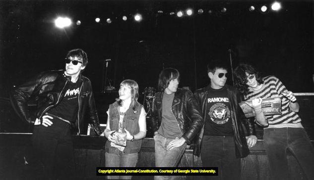 A young teenager smiling as she stands with four men in front of a stage.