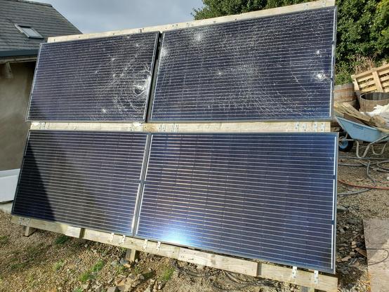 Array of 4 solar panels in a recently upended and righted homemade wooden stand, the glass on the upper two is smashed