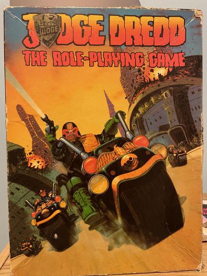 Cover of the "Judge Dredd: The Role-Playing Game," featuring vibrant artwork of the character on his futuristic motorcycle with other Judges in a dynamic chase, shooting. The title is prominently displayed at the top.