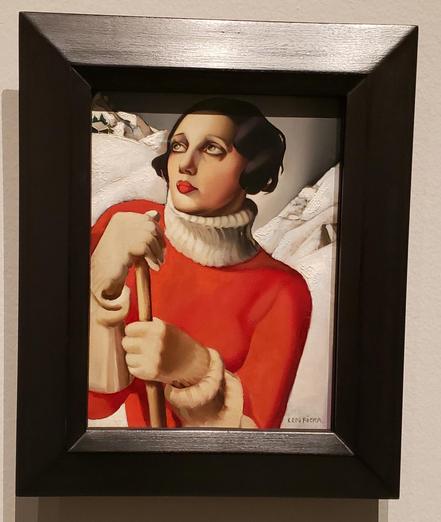 Small painting in a black frame of a woman with short black hair and a red and beige sweater, with dark and light snow and sky. 