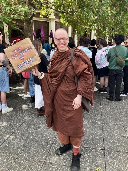 Venerable Pasanna in brown robes marching with placcard "may all beings be happy"