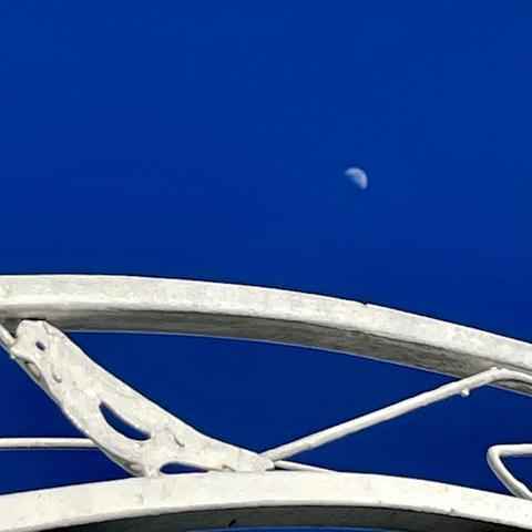 A partial view of the moon is seen in a clear blue sky, framed by white structures in the foreground.