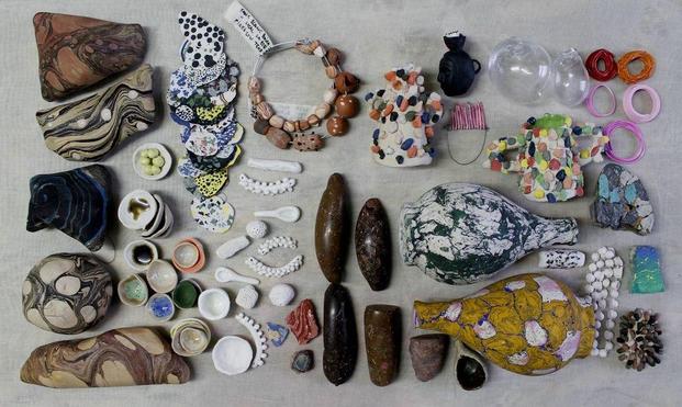 Image: photo from above of various objects, some of which my be rocks / stones; there is a pair of bracelets top middle, for example, that seems to employ stones, but the label attached –  in Catalan and English – suggest that they were “fired low temp”; the are small white spoons, polished stones, what seems to be transparent plastic shapes that are somewhat biomorphic, loops of stuff, etc. • “Dún Laoghaire-Rathdown County Council is delighted to present an exhibition of new works by Vanessa Donoso López – A rock can hurt you, a rock can open a nut. Over recent years working across Ireland and Spain, Vanessa Donoso López has shaped her latest installation – a gathering of works deeply rooted in the land, its people and their shared cultural heritage. This collection, comprising over 1,000 pieces includes archaeological artefacts and a series of marbled shapes that echo the intricate patterns found on petrified objects and rocks…”