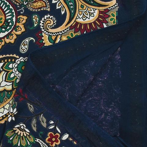 Navy jersey fabric with a busy paisley print on top in mustard yellow with white, blue, and dark green accents. A corner is turned over to show dark navy "wrong" side of the fabric.