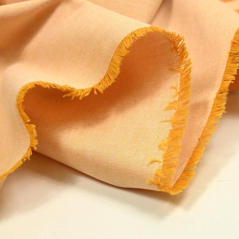 Oxford cotton in orange, showing the edge of the fabric. Here the weft is orange, and wrap is white.