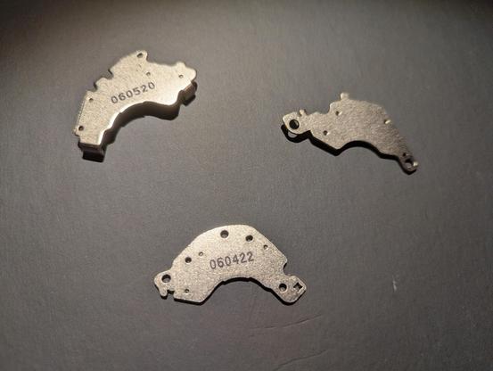 Three metal magnet pieces in various shapes, with holes for screws. Two have numbers printed on them. They're all vaguely crescent shaped as they're meant to fit into a corner.