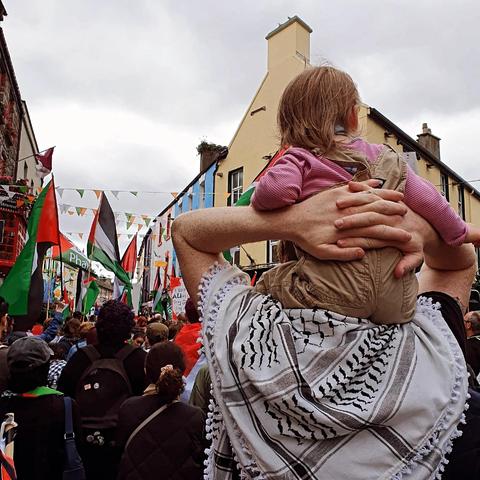Denman standing with his child on his shoulders in a crowd marching through Galway city.
