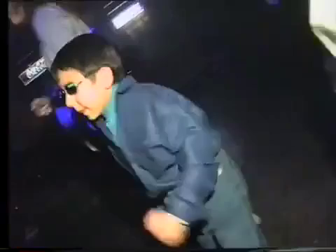 Video gif. Young boy in sunglasses and adult attire, dancing and boogeying amongst adults in a dark nightclub.