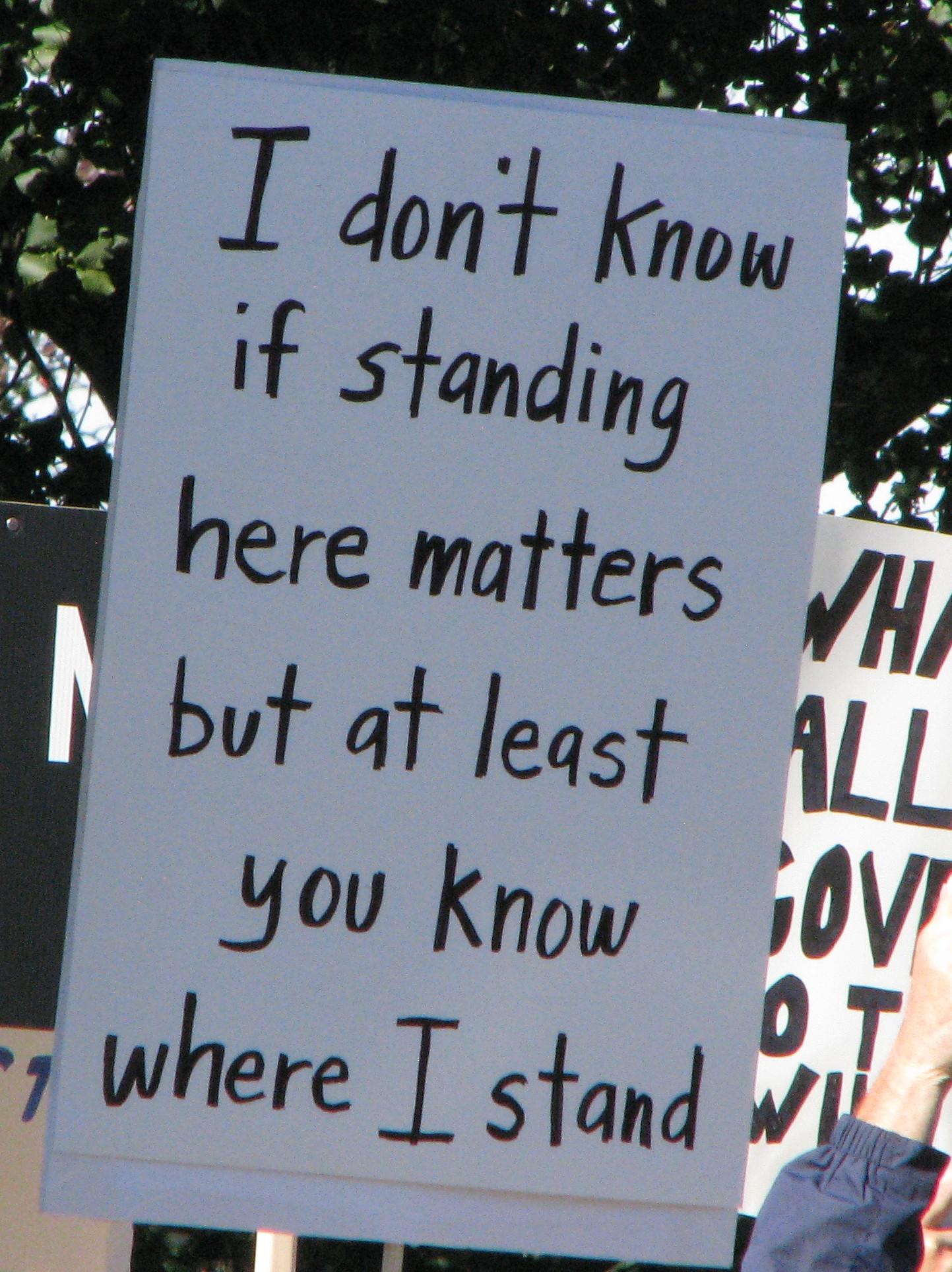 A protest sign. Black text on white which reads "I don't know if standing here matters but at least you know where I stand"