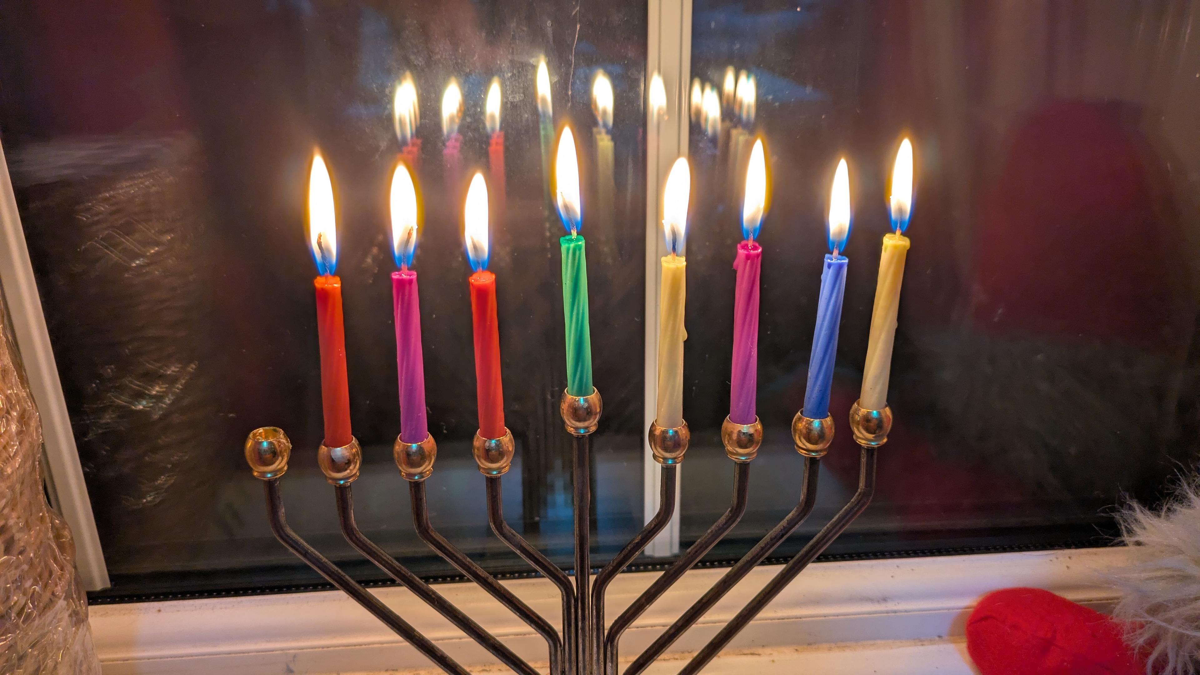 A chanukiah with eight differently-coloured lit candles.