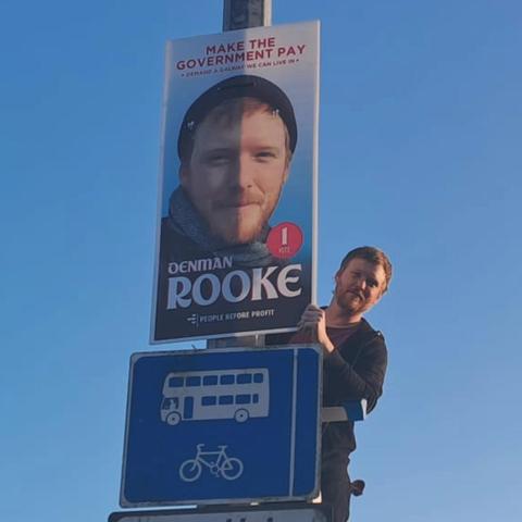 Denman on a ladder next to a big poster of his head