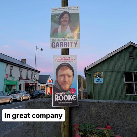 Two posters up on poles in Oughterard. One of Denman Rooke and one of Sheila Garrity with text saying "In Great Company"