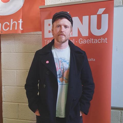 Denman Rooke standing in front of a BÁNÚ pull up banner