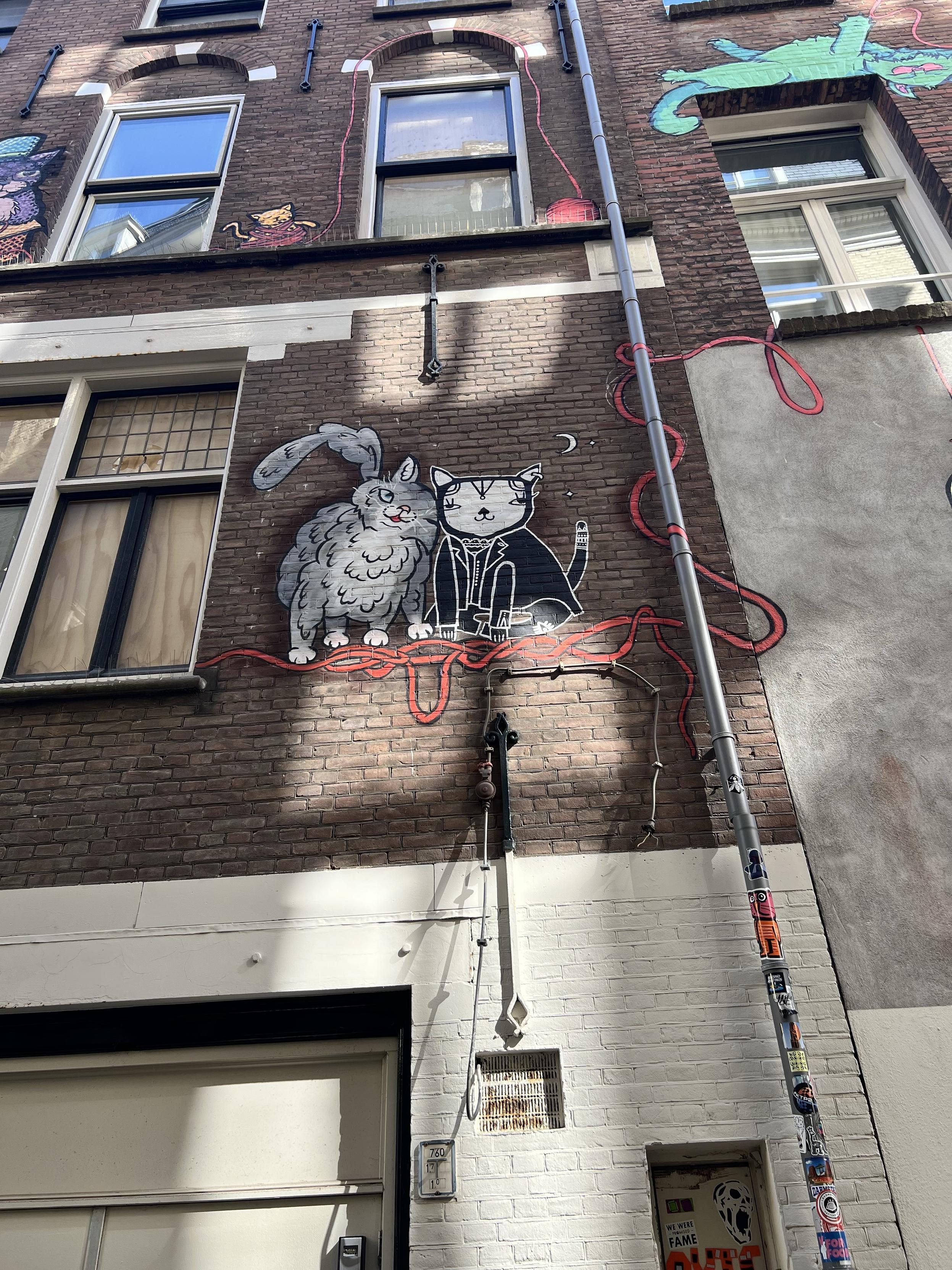 Street art of two cats cuddled up, one fluffy and on wearing a leather jacket.