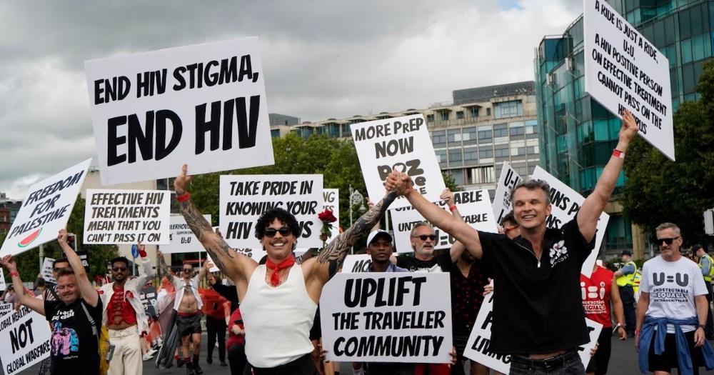 HIV organisation Poz Vibe Tribe marching in Dublin Pride. Participants hold banners in the air with black text on white backgrounds.