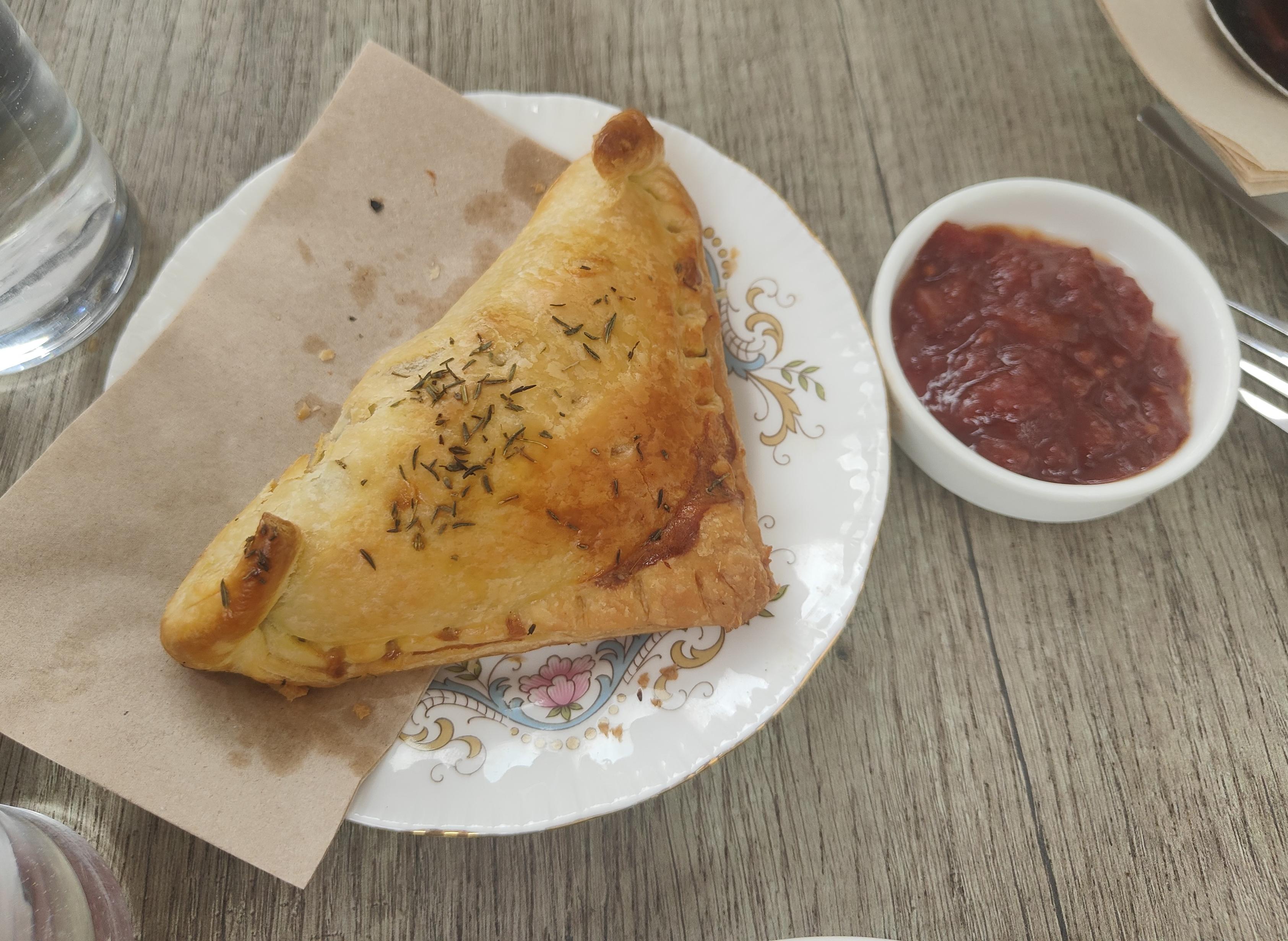 A photo of a pastry parcel, which has a mushroom filling, and a small pot of tomato relish.