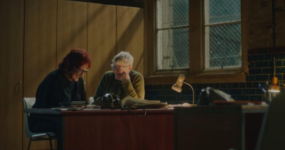 A still from the Lesbian Lines documentary showing two former helpline volunteers chatting and laughing at a desk.