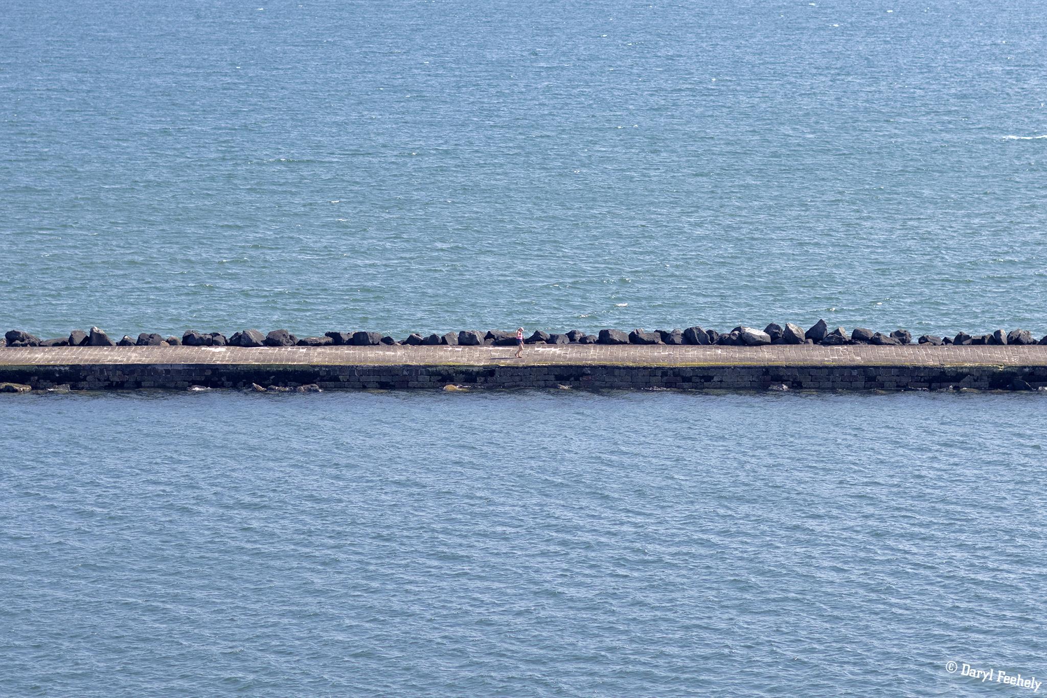 A walker on the walkway towards Poolbeg Lighthouse.
