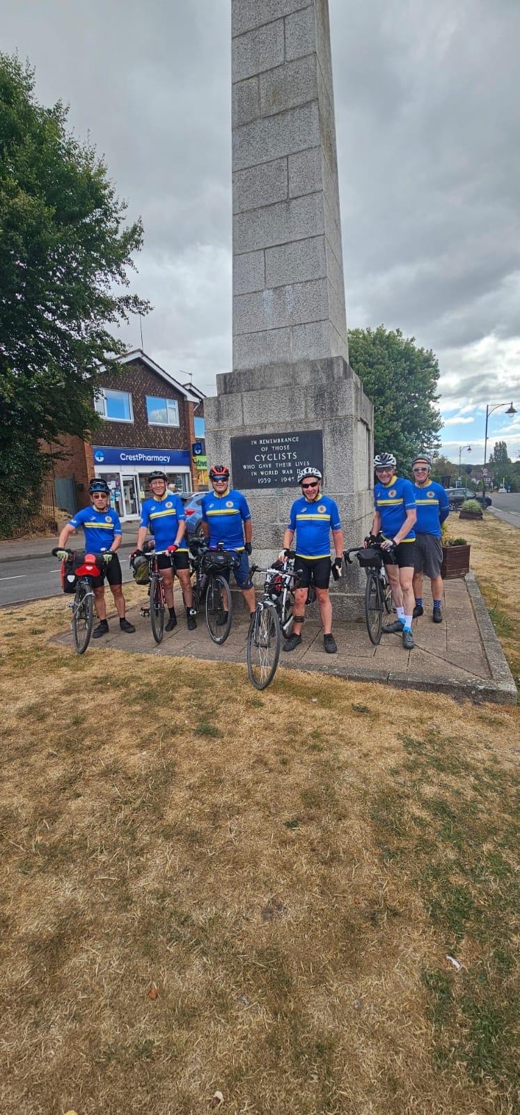 Six cyclists standing in front of a cyclist’s war memorial in Meriden