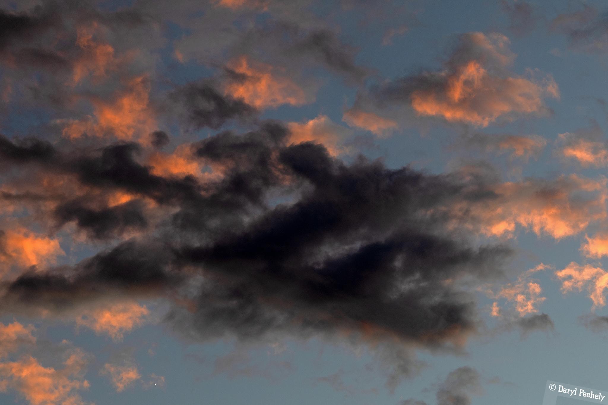 A dark cloud covers orange sunset clouds.