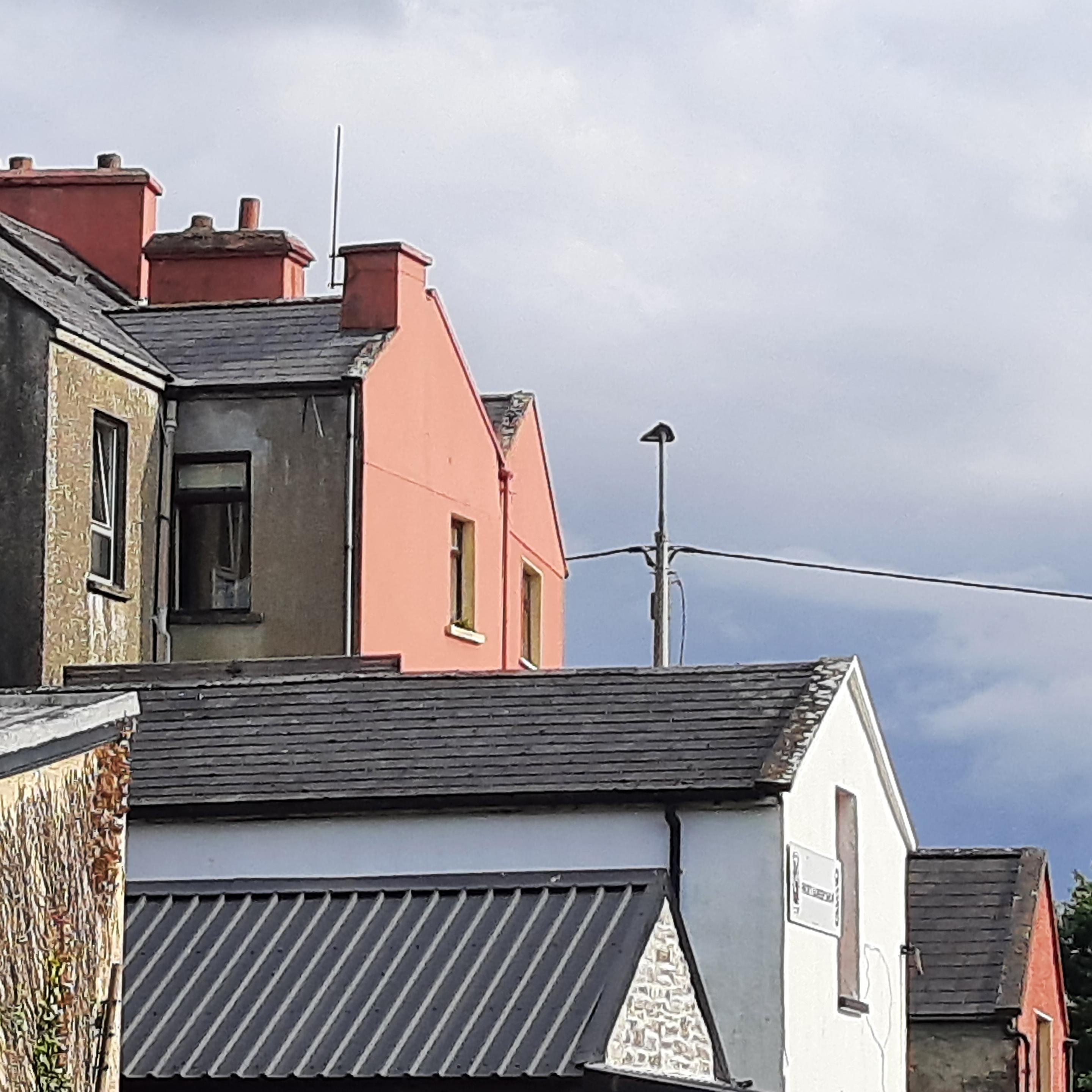 A square photo showing three plain multistorey old small-town houses with single-storey extensions at various heights protruding into backyards.