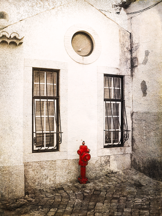 A bright red fire hydrant stands out against a white-washed facade in a cobblestone street in Alfama, Lisbon's oldest quarter.