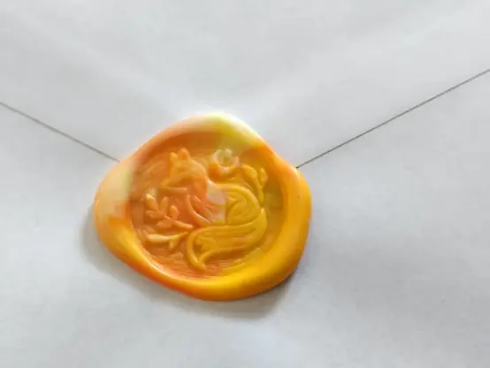 An wax seal with a fox made of different shades of orange.