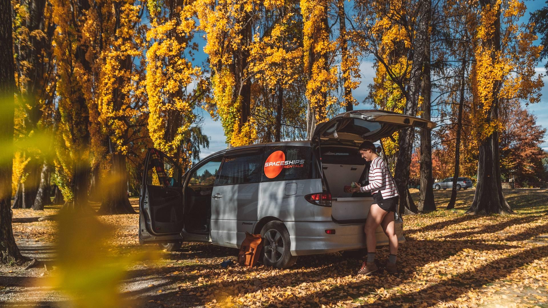 Spaceships campervan parked in a forest - autumn colours so brown, yellow and orange leaves. Space Traveller is getting items from the boot and is preparing for a hike on this sunny autumn day.