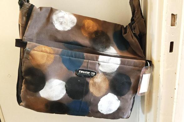 Vaaleanruskea pehmeä olkalaukku, johon on spraymaaliöla maalattu valkoisia, sinisiä, mustia ja kullavärisiä palloja.